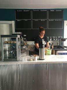 Picture of coffee station with blank menu and one woman filling a bag.
